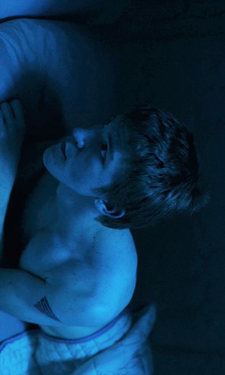 a shirtless man laying in the dark with his arm wrapped around another person's chest