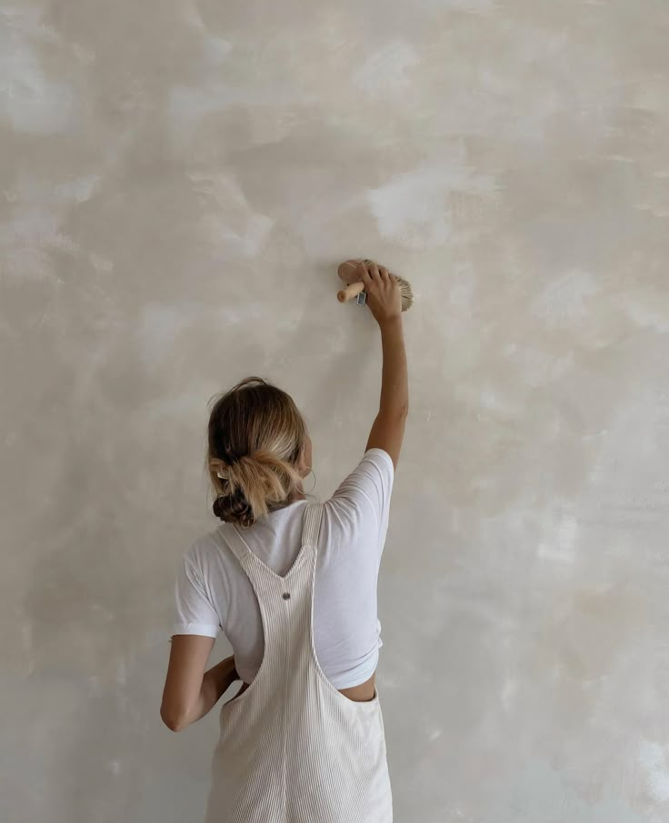 a woman is painting the wall with white paint and she has her hands up in the air