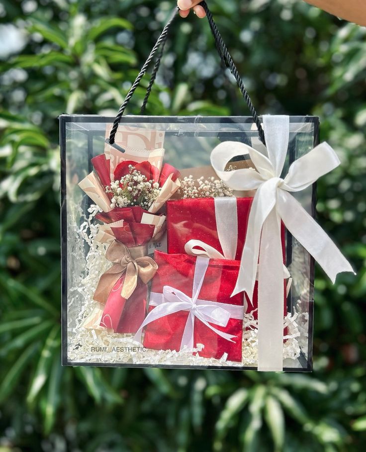 a clear box filled with red and white wrapped gift boxes in front of some trees