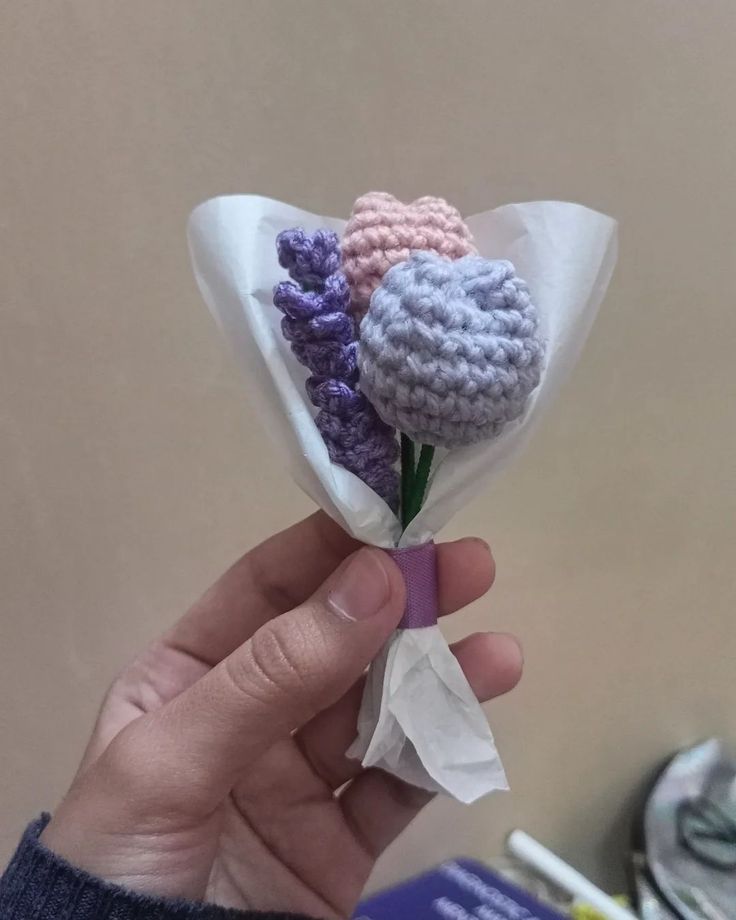 a person holding a crocheted flower in their left hand, with the end of it wrapped in tissue paper