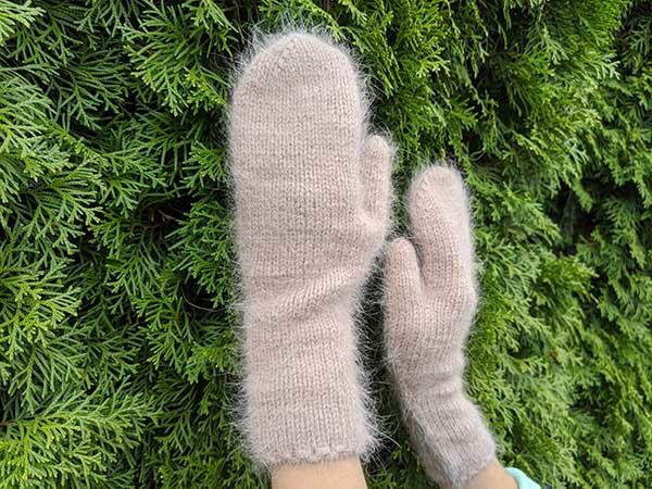 someone's hands wearing mittens and gloves in front of green plants