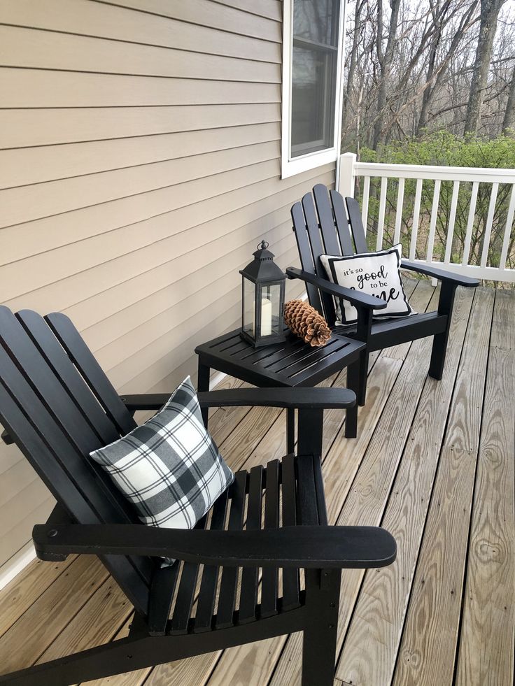 two black chairs sitting on top of a wooden deck next to a lamp and pillow