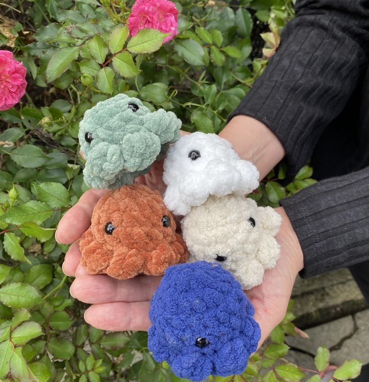 four small crocheted animals are held in someone's hand with pink flowers behind them