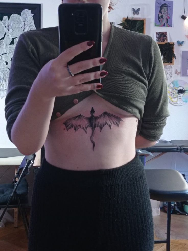 a woman holding a cell phone in front of her stomach with a bat tattoo on it