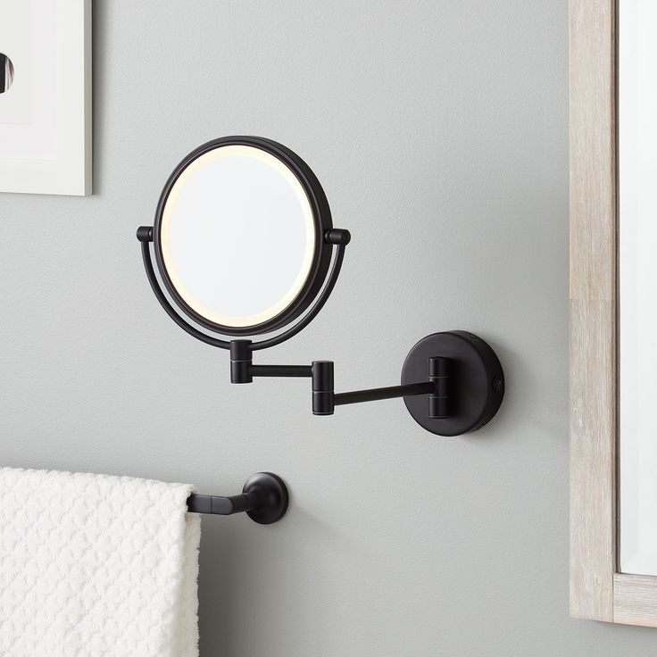 a bathroom mirror mounted to the side of a wall next to a white towel rack