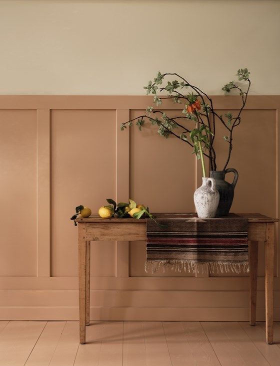 a wooden table topped with a vase filled with flowers and fruit next to a wall