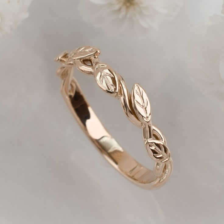 a gold wedding ring with leaves on it and flowers in the background, close up