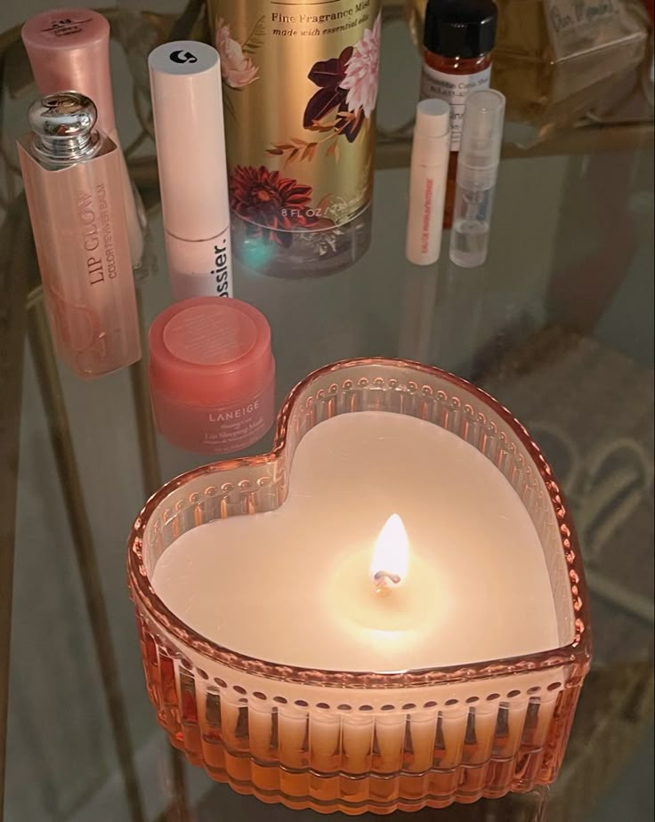 a heart shaped candle sitting on top of a glass table next to bottles and candles