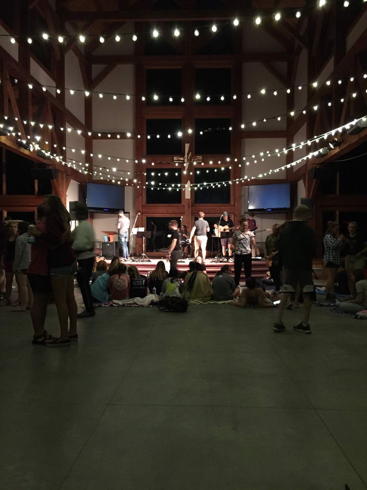 a group of people standing and sitting in a room with lights hanging from the ceiling