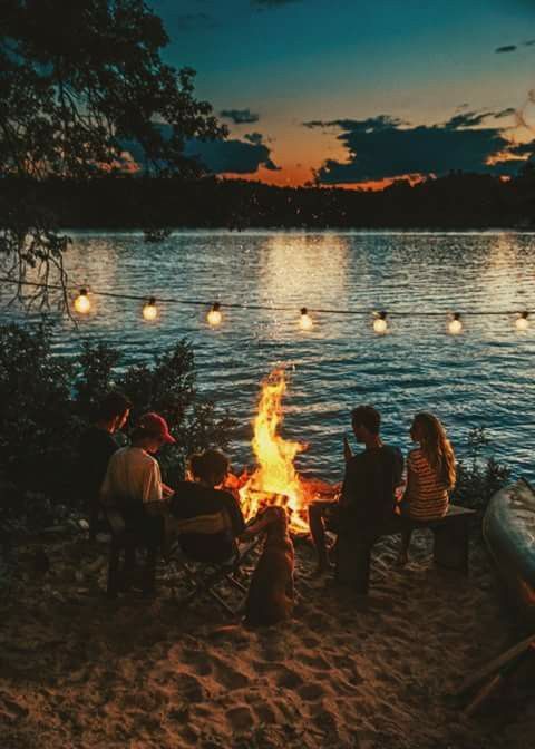 people sitting around a campfire on the beach at night with lights in the sky