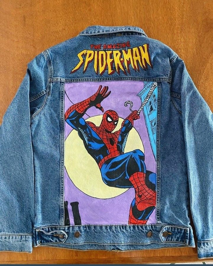 a jean jacket with the image of spider - man on it, hanging from a shelf