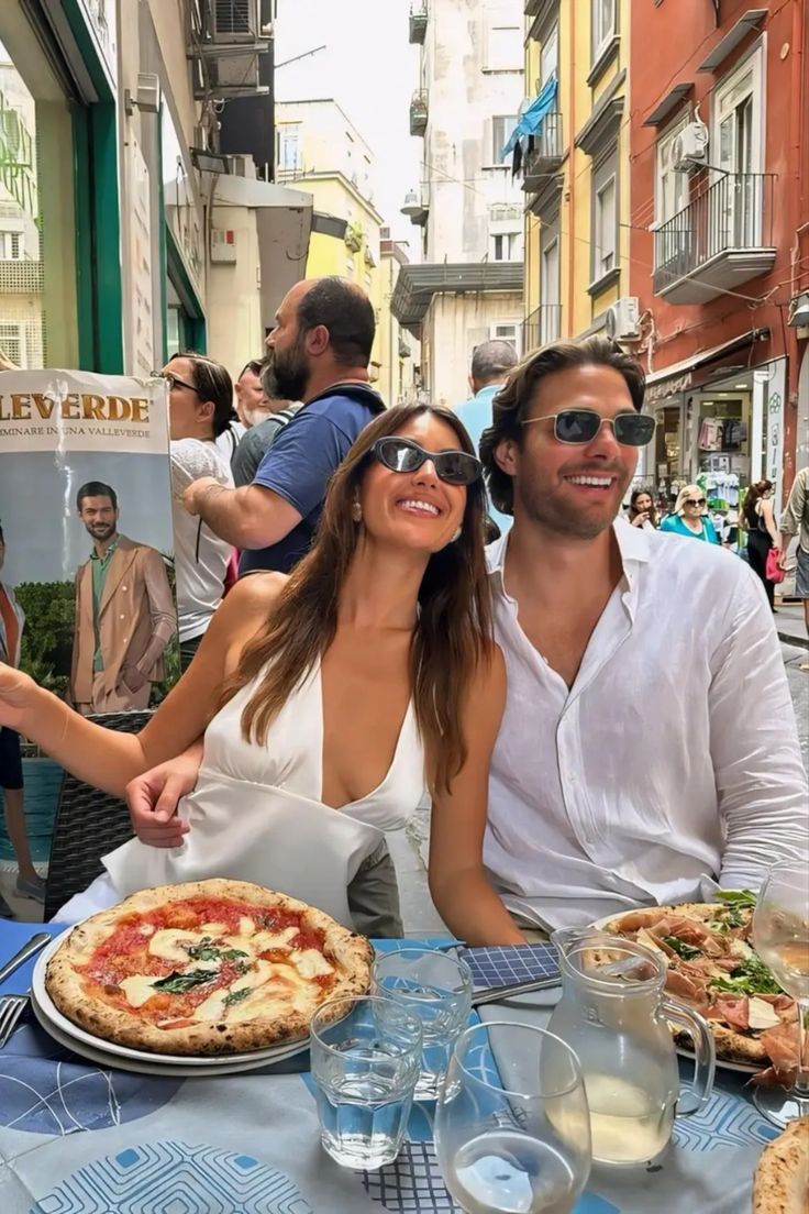 two people sitting at an outdoor table with pizza