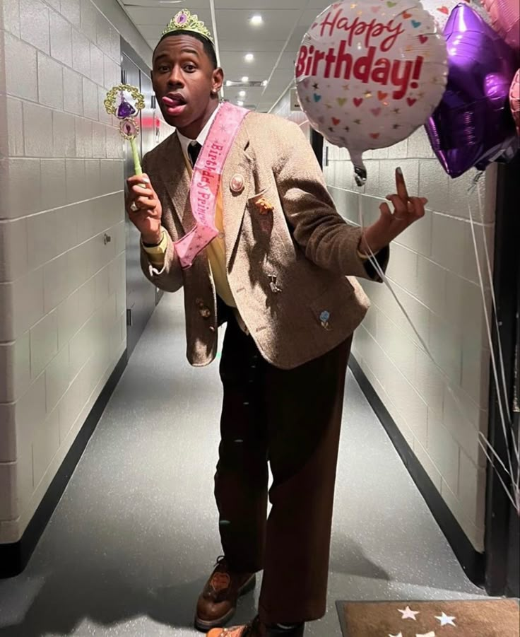 a man in a suit is holding balloons and pointing to the side while walking down a hallway