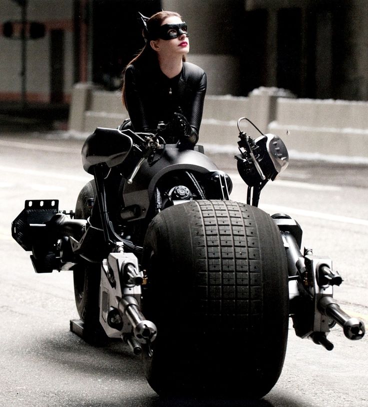 a woman riding on the back of a motorcycle down a street with her catwoman costume