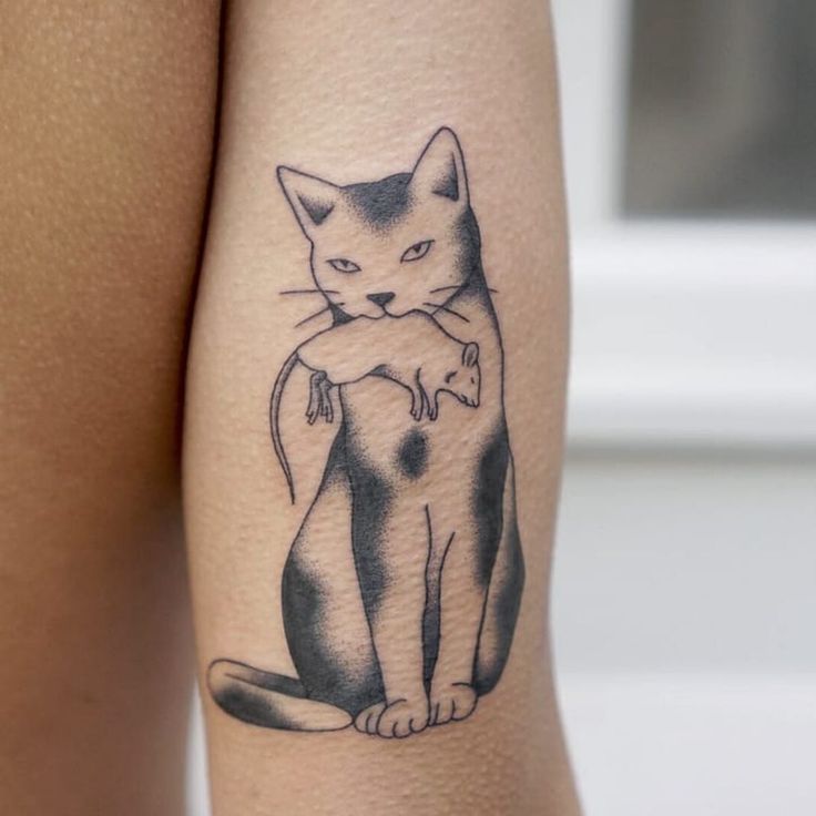 a cat tattoo on the leg of a woman's thigh, with an image of a cat holding a mouse