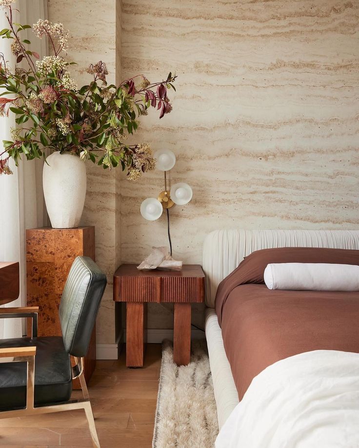 a bed sitting next to a wooden table with a vase on top of it near a chair