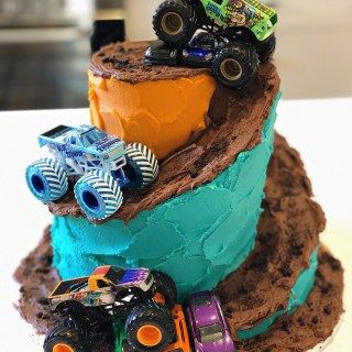 a birthday cake decorated with monster trucks and dirt on the top tier is blue, green, and brown icing