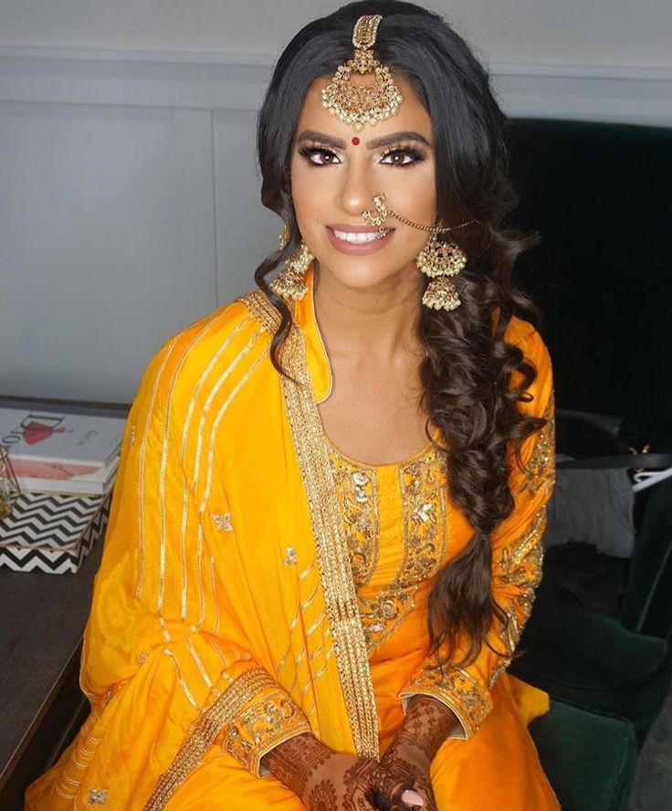 a woman in an orange outfit with henna on her face and hands, smiling at the camera