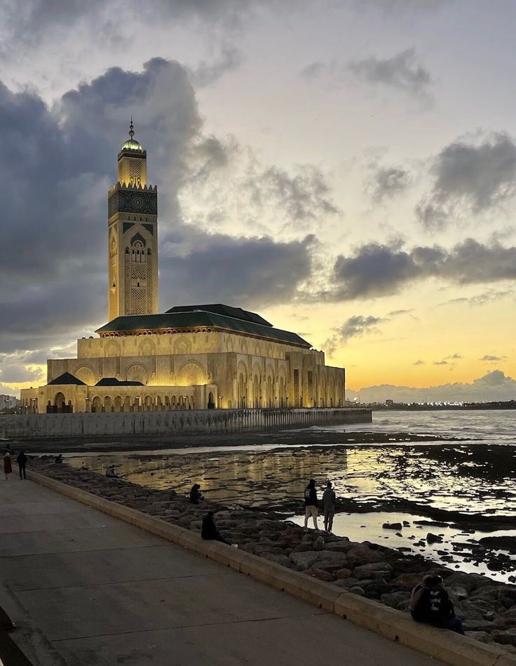 a large building sitting on top of a beach next to the ocean at sunset with people walking around it