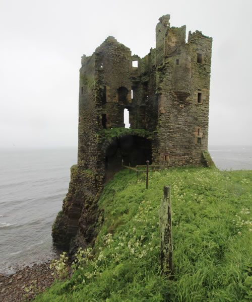 an old stone castle sitting on top of a lush green hillside next to the ocean