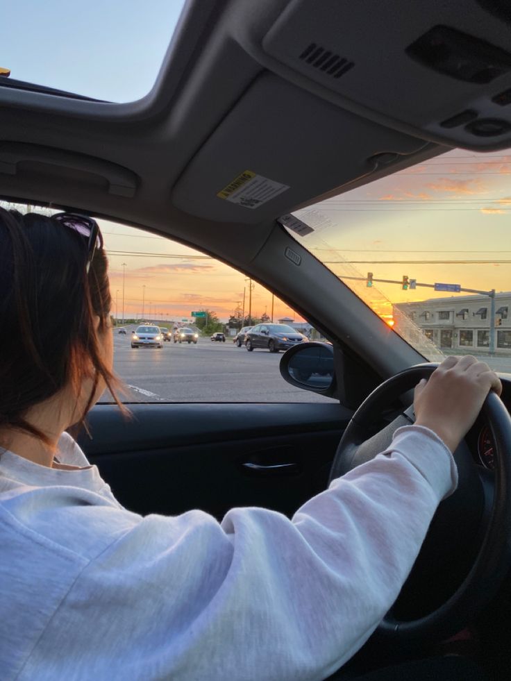 a woman is driving her car in the parking lot at sunset or dawn, looking out the window