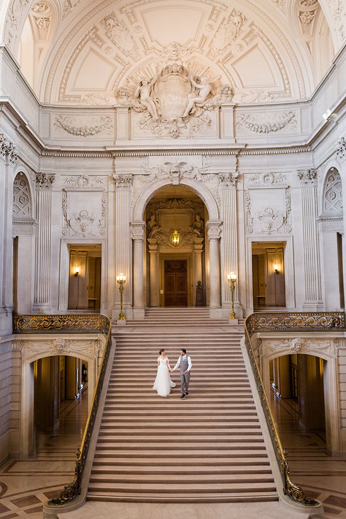 a bride and groom are standing on the stairs in an ornate building with chandeliers