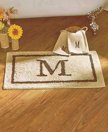 a bathroom rug with the letter a on it next to a bathtub and flowers