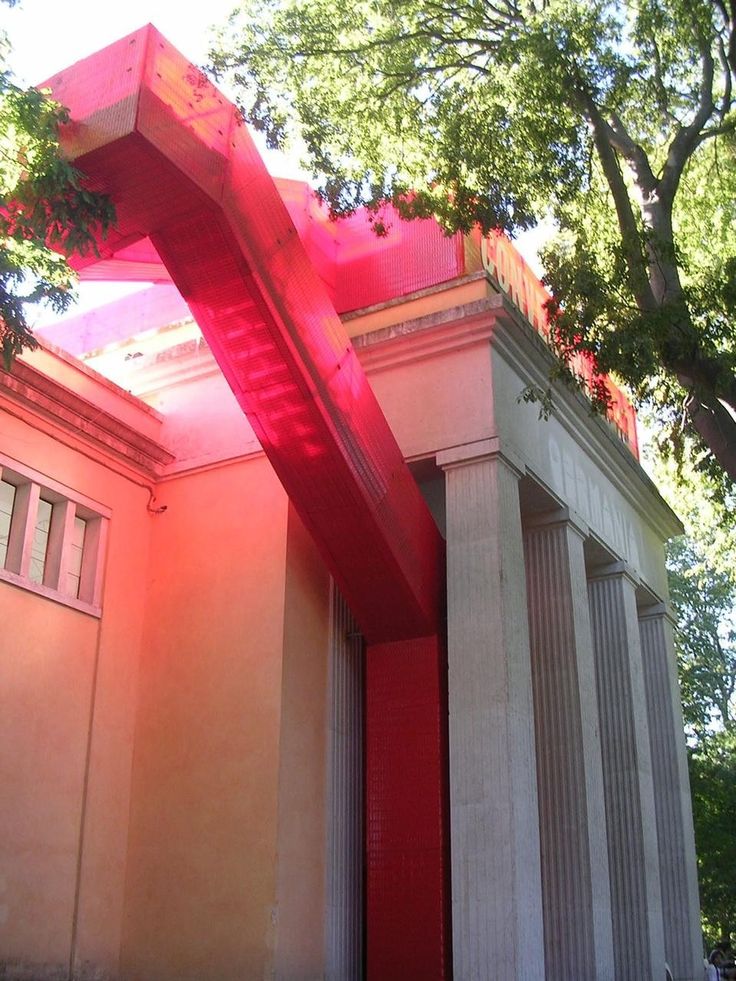 a large red object sitting on the side of a building next to a tall tree