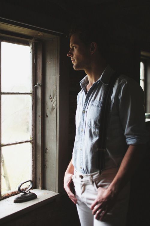 a man standing in front of a window with his hands on his hips and looking out the window