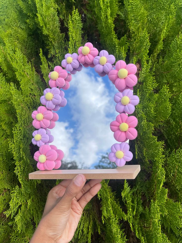 a hand holding up a mirror with flowers in the shape of a wreath on it