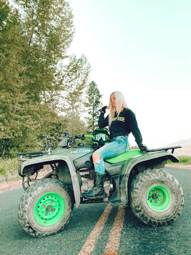 a woman sitting on top of an atv in the middle of a road with trees behind her