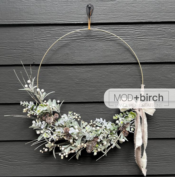 a wreath with white flowers and greenery hanging on the side of a wooden wall