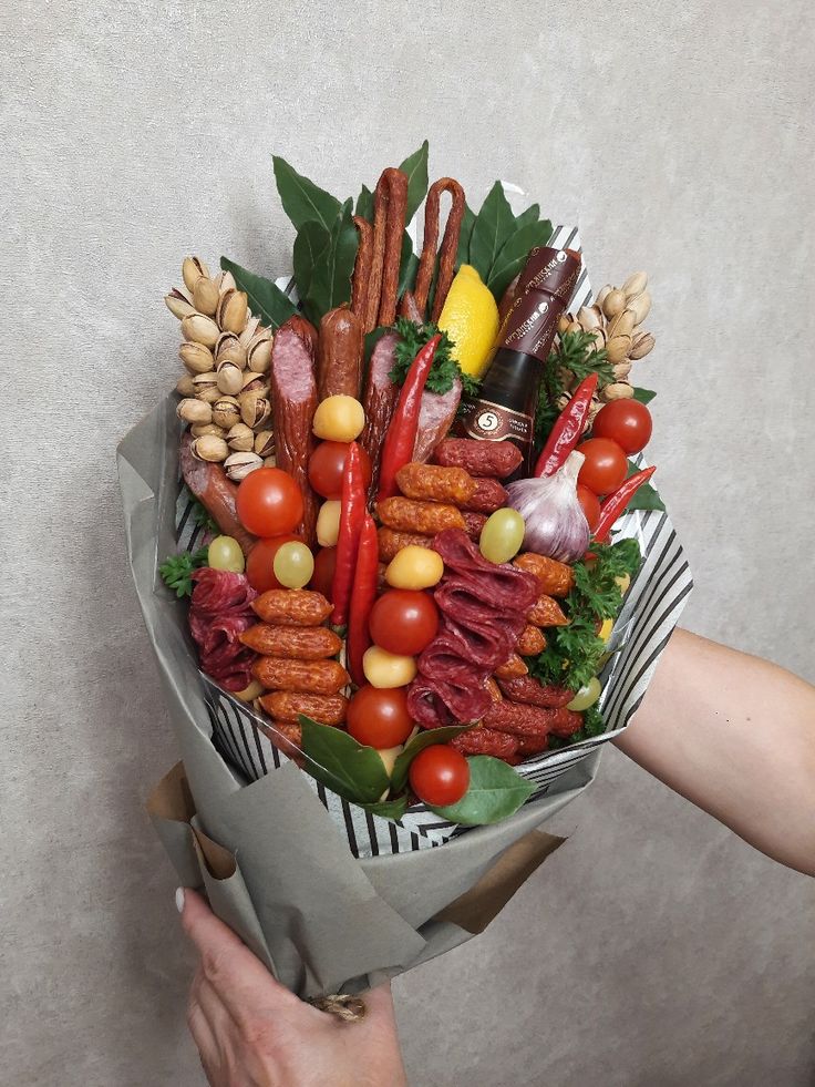 a bouquet of vegetables and meats is held by someone's hand in front of a wall