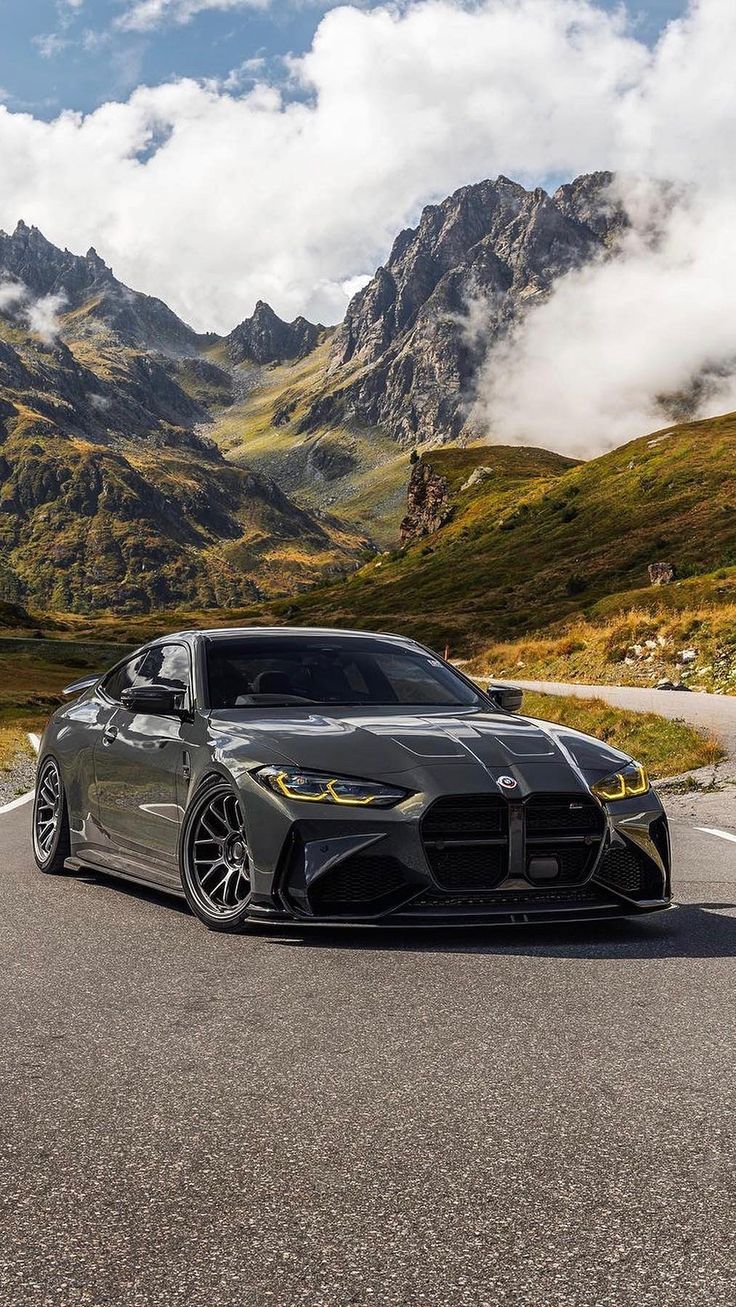 a grey sports car driving down the road with mountains in the backgrouund