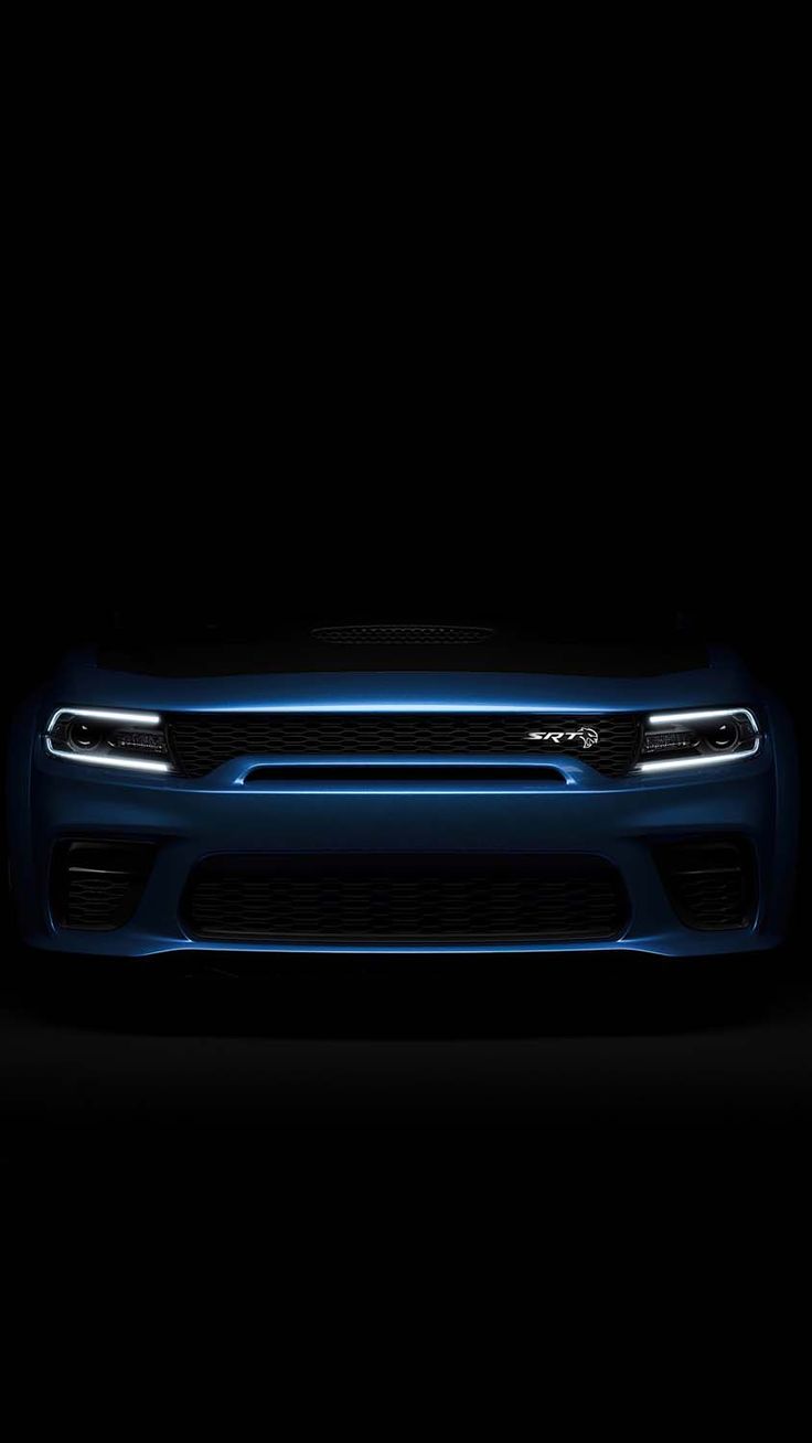 the front end of a blue dodge charger parked in a dark room with its lights on