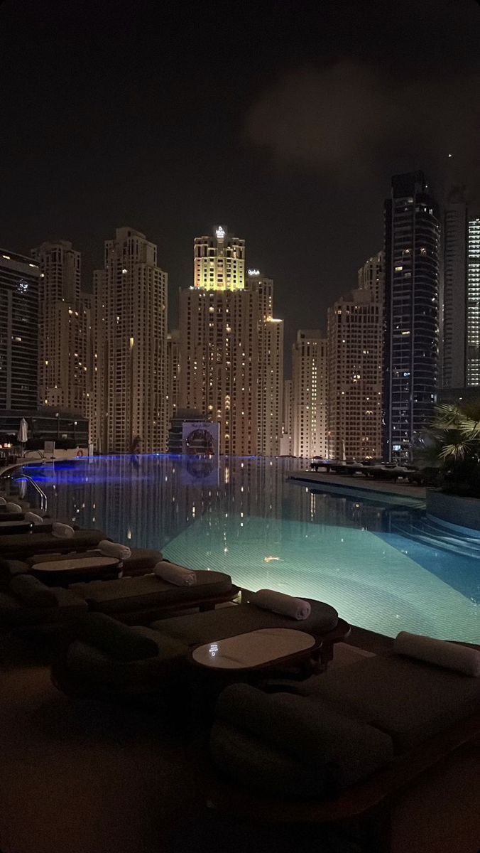 an outdoor swimming pool with lounge chairs and city lights in the background