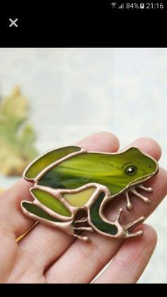 a green frog brooch sitting on top of a persons hand