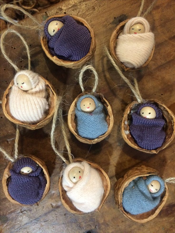 six small knitted nativity ornaments hanging from twine strings on a wooden table