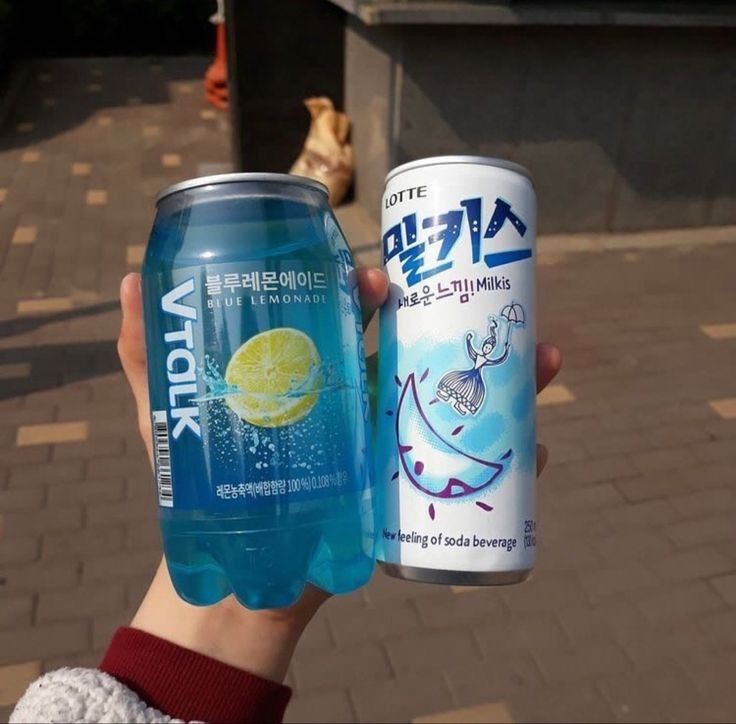 a person holding up two cans of soda