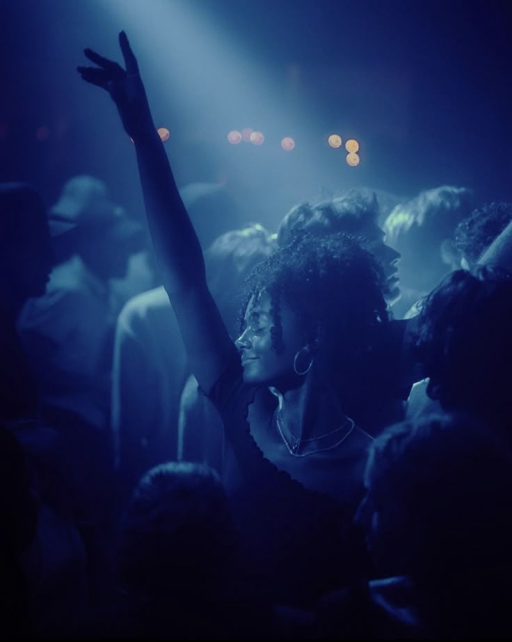 a woman standing in the middle of a crowd at a concert with her arms up