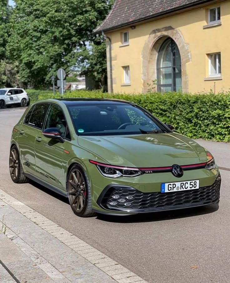 a green car is parked on the side of the road next to a house and bushes