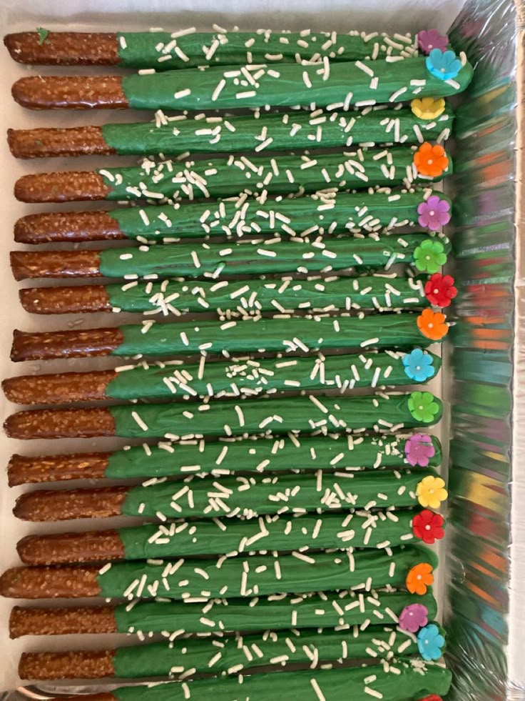 a box filled with green sticks covered in white frosting and sprinkles