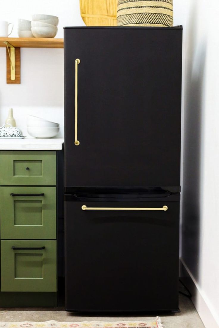 a black refrigerator in a kitchen next to green cabinets and white counter tops with gold handles