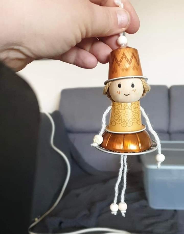 a person holding a bell ornament with a small doll on it's side