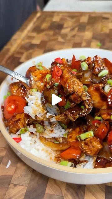 a white plate topped with meat and vegetables on top of rice next to a wooden cutting board