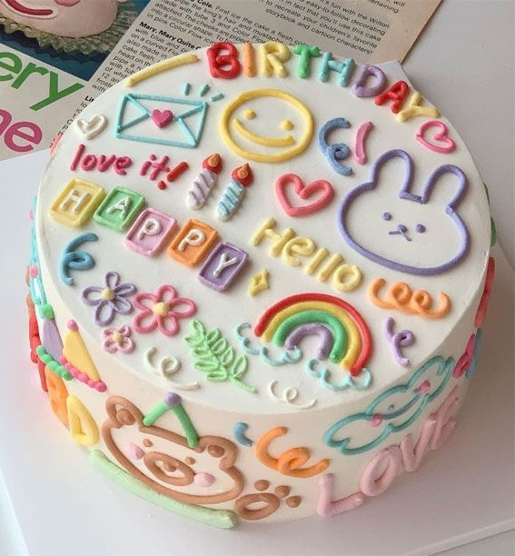 a decorated birthday cake sitting on top of a table next to a book and cup