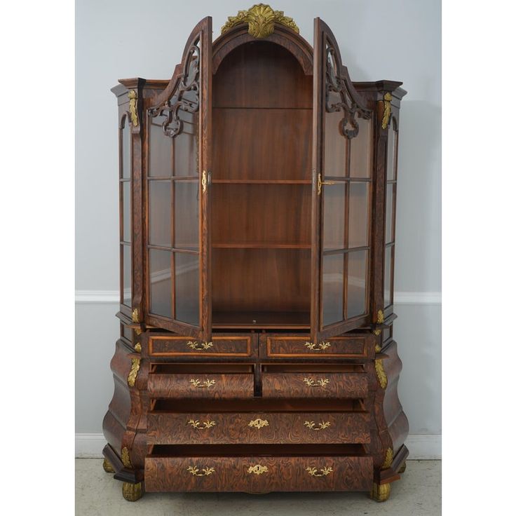 an antique wooden desk with glass doors and gold trimmings on the top shelf