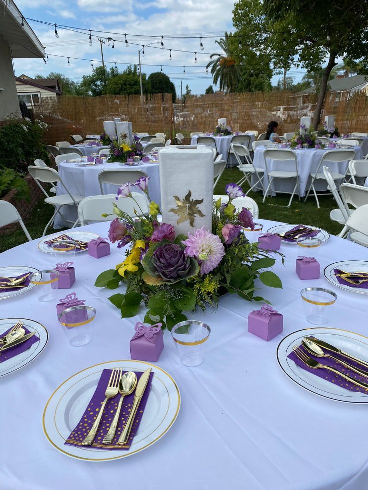 the table is set with purple and white plates, napkins, silverware, and flowers