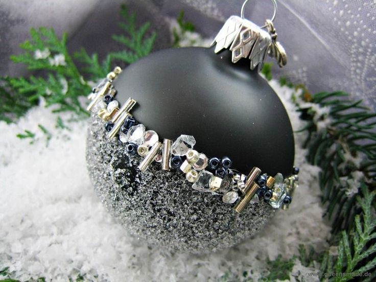 a black ornament with silver and crystal beads on it sitting in some snow