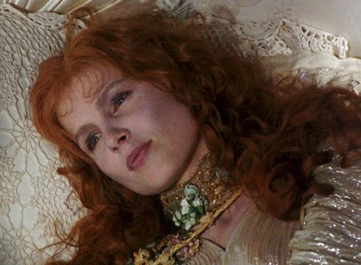 a woman with red hair laying down on a white bed next to a lace curtain